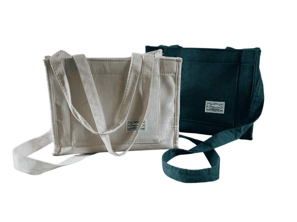 Cream and dark green corduroy tote bags with front pockets and long straps displayed side-by-side against a transparent background.